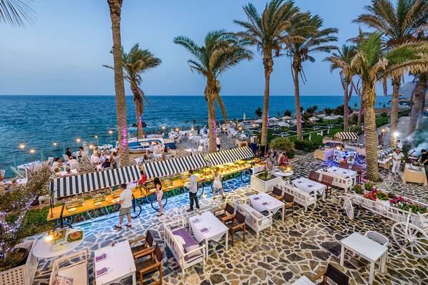 Luftaufnahme des Minos Imperial Beach Resorts mit Außenbereich, Tischen, Palmen und Meer.