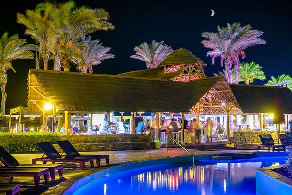 Pool und Bar im Minos Imperial Beach Resort bei Nacht mit Palmen und Gästen.