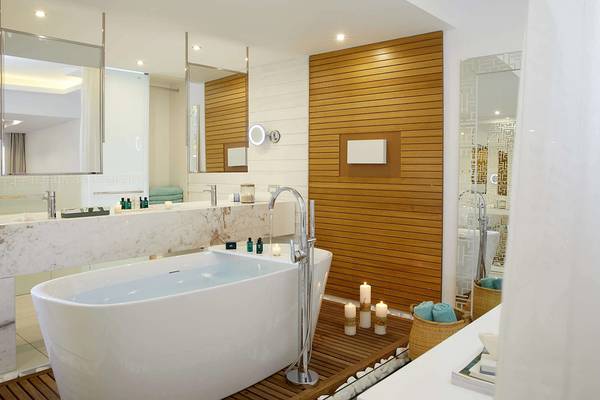 Ein elegantes Badezimmer mit Badewanne, Holzwand und Spiegeln im Minos Imperial Beach Resort.