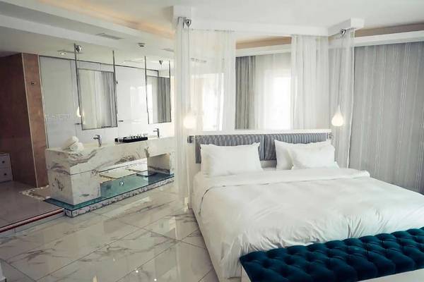Schlafzimmer im Minos Imperial Beach Resort mit weißem Bett, Marmorboden und Badewanne.