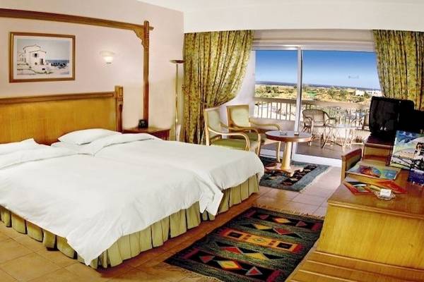 Doppelzimmer im Hurghada Long Beach Resort mit Balkon, zwei Betten, Schreibtisch, Fernseher und Blick auf eine Terrasse.