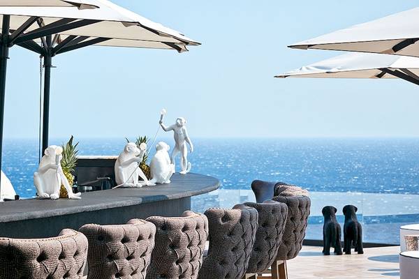 Barbereich des Royal Myconian Resorts mit Blick auf das Meer und weißen Affenstatuen.