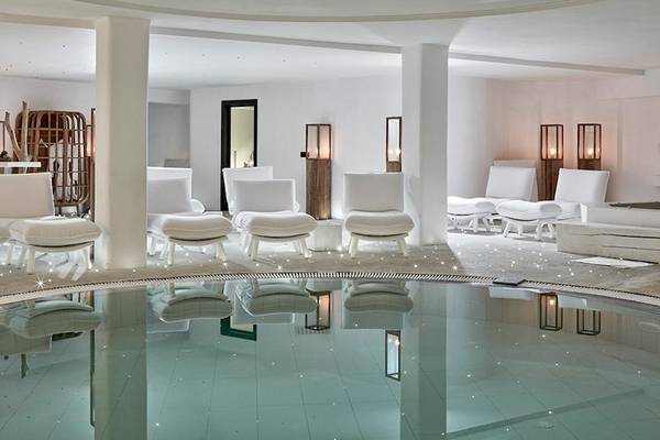 Innenbereich des Royal Myconian Resorts mit Pool, weißen Möbeln und weichen Kissen.