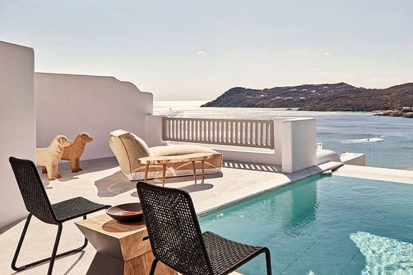 Royal Myconian Resort Balkon mit Pool und Meerblick, Hundestatue und Loungesofa.