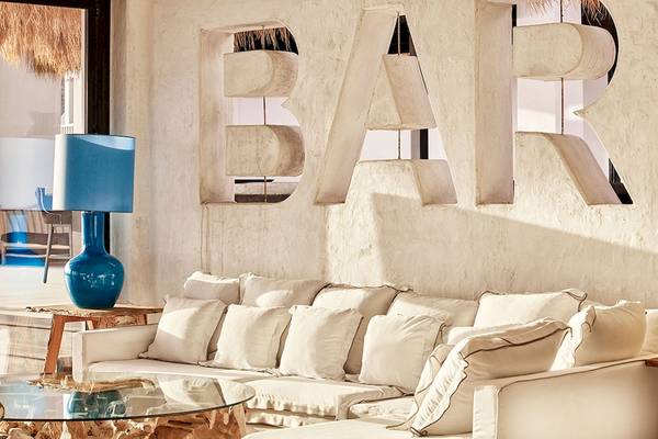 Lounge-Bereich im Royal Myconian Resort mit einem weißen Sofa, Lampen und einer Wand mit dem Wort 'BAR'.