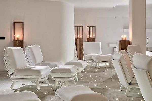 Weißer Loungebereich im Royal Myconian Resort mit weißen Sesseln, runden Hockern und brennenden Kerzen.