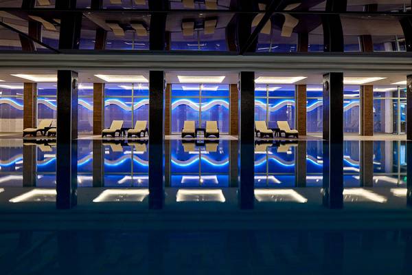 Innenpool des Porto Bello Royal Hotels mit blauen Lichtern und weißen Liegen.