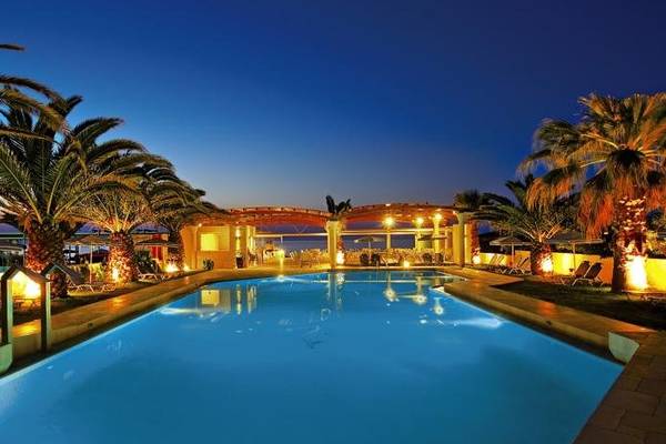 Der Poolbereich des Eva Bay Hotels bei Nacht mit Palmen und beleuchteten Liegestühlen.