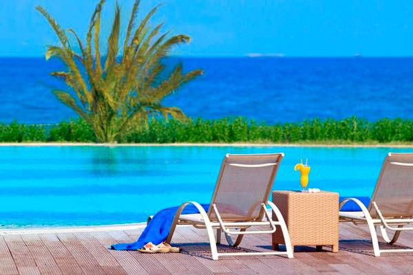 Pool-Lounge-Bereich im Astir Odysseus Kos Resort & Spa mit zwei Liegen und einem Tisch.