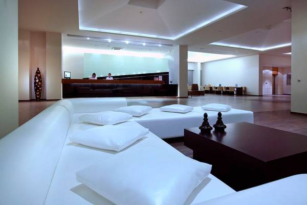 Hotellobby mit weißen Sofas, Kissen und einem dunklen Tisch vor einer Rezeption.