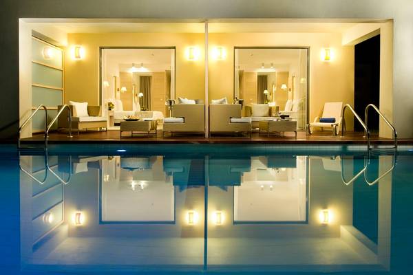 Pool-Loungebereich im Astir Odysseus Kos Resort & Spa mit reflektierten Lichtern und Möbeln.