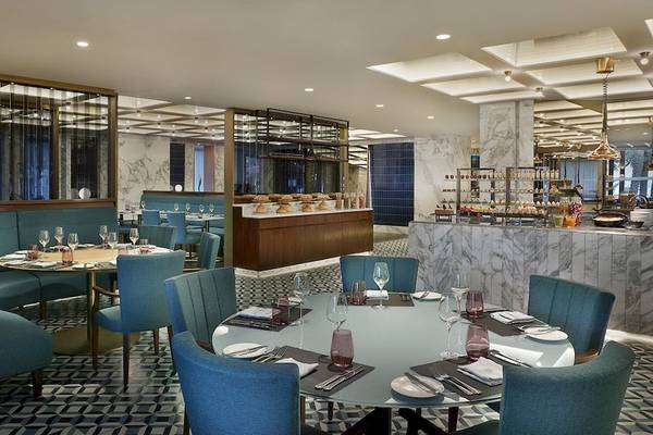 Innenraum des Al Bustan Palace, A Ritz Carlton Hotel mit blauen Stühlen und Tischen, Marmorboden und einer Bar.