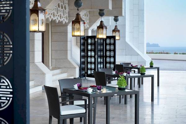 Außenbereich des Al Bustan Palace, A Ritz Carlton Hotel mit gedeckten Tischen und dekorativen Lampen.