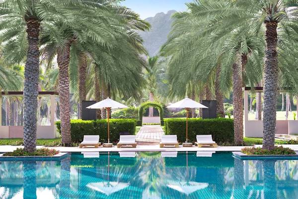 Außenpoolbereich des Al Bustan Palace Hotels mit Liegestühlen und Sonnenschirmen.