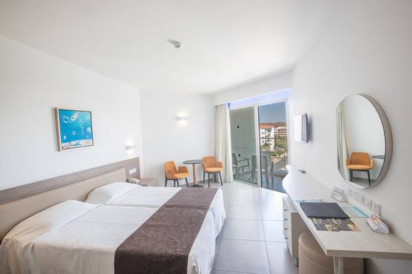 Innenansicht eines Zimmers im Vassos Nissi Plage Hotel mit zwei Betten, einem Schreibtisch und einem Balkon.