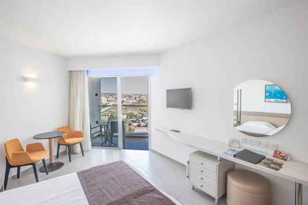 Innenansicht eines Hotelzimmers im Vassos Nissi Plage mit Bett, Schreibtisch und Terrassenzugang.