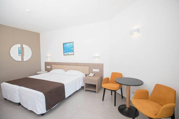 Ein modernes Hotelzimmer im Vassos Nissi Plage Hotel mit zwei Betten, Nachttischen und Stühlen.