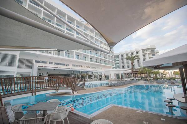 Poolbereich des Vassos Nissi Plage Hotels mit Liegestühlen und Gebäuden im Hintergrund.