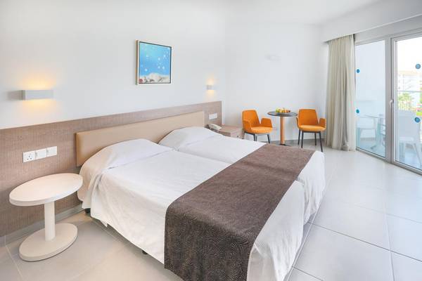 Ein modernes Hotelzimmer im Vassos Nissi Plage mit zwei Betten, einem Tisch und Stühlen vor einer Glastür.