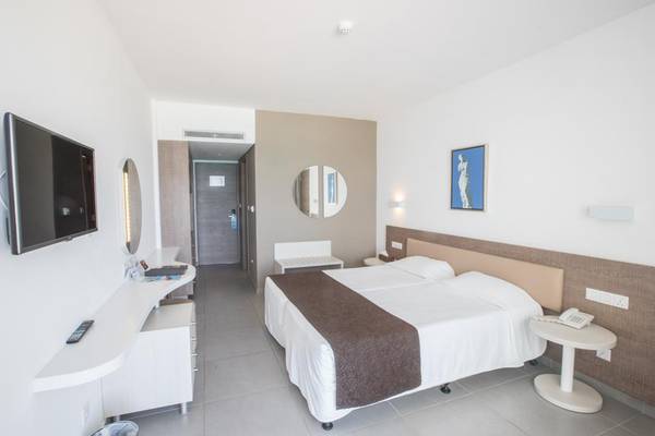 Hotelzimmer im Vassos Nissi Plage mit Doppelbett, Fernseher, Spiegel, und Nachttisch.
