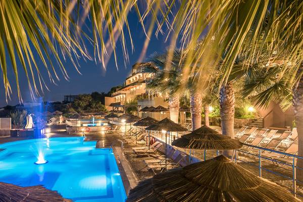 Der Pool des Blue Bay Resorts bei Nacht mit beleuchteten Palmen und Sonnenliegen.