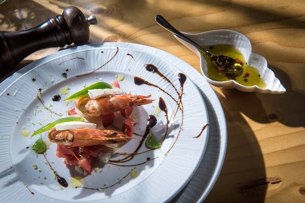 Ein weißer Teller mit Garnelen, Wassermelone und Mozzarella auf einem Holztisch.