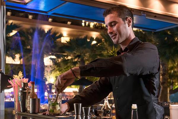 Ein Barkeeper im Blue Bay Resort bereitet einen Cocktail zu, während er lächelt.