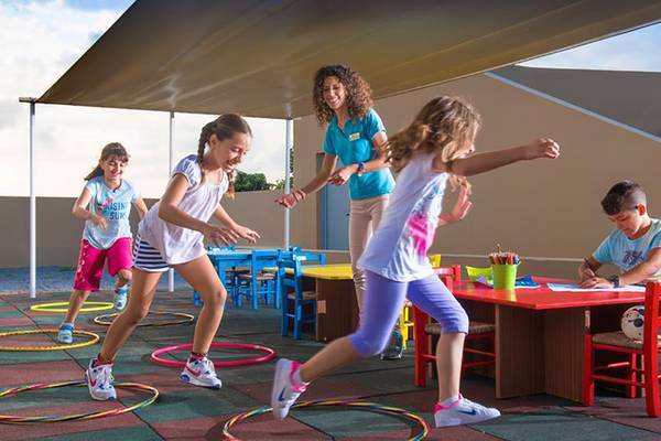 Kinder spielen im Freien im Blue Bay Resort, begleitet von einer Frau.