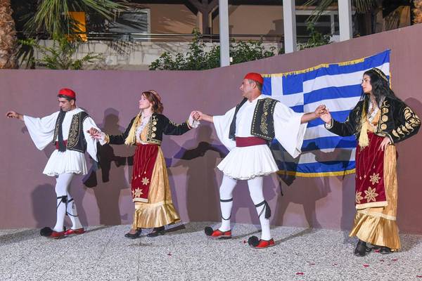 Vier Tänzerinnen und Tänzer vor einer griechischen Flagge beim Blue Bay Resort.