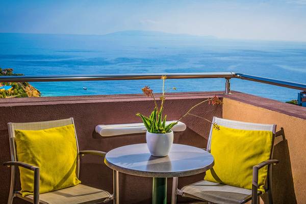 Terrasse mit Meerblick im Blue Bay Resort mit zwei Stühlen, einem Tisch und einer Pflanze in einer Vase.