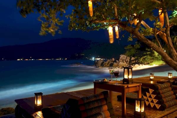 Dinner am Strand unter einem Baum mit brennenden Laternen bei Nacht.