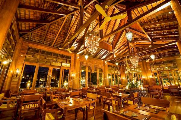 Innenbereich des Restaurants im Santhiya Koh Phangan Resort mit Holzmöbeln, Kronleuchtern und einer abendlichen Atmosphäre.