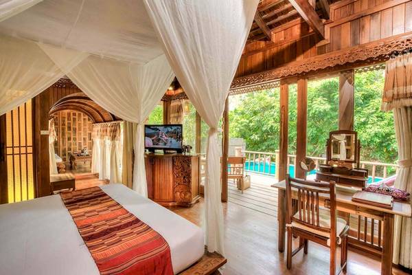 Zimmer im Santhiya Koh Phangan Resort & Spa mit Bett, Fernseher, Schreibtisch und Pool im Hintergrund.