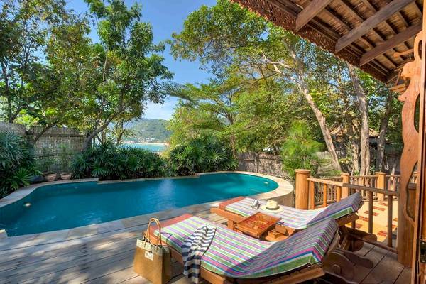 Ein Swimmingpool auf einer Holzterrasse des Santhiya Koh Phangan Resorts mit Lounge-Stühlen und Blick auf den Ozean.