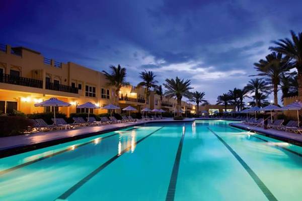 Al Hamra Village Hotel Pool bei Nacht mit Lounge-Stühlen und Sonnenschirmen.