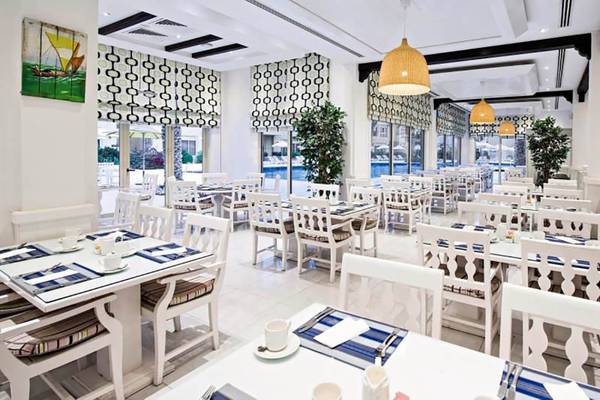 Innenansicht des Restaurants im Al Hamra Village Hotel mit weißen Tischen und Stühlen.