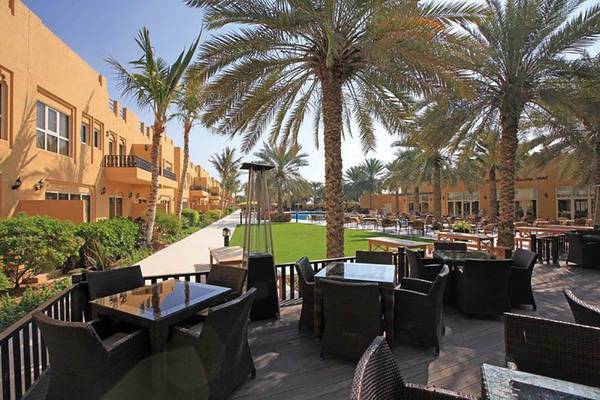 Terrasse des Al Hamra Village Hotels mit Tischen, Stühlen und Palmen