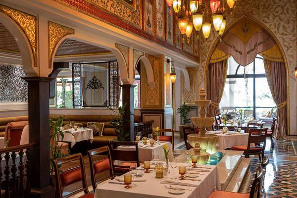 Innenbereich des Restaurants im Jumeirah Zabeel Saray mit dekorativ beleuchteten Decken, hängenden Kronleuchtern, einem Brunnen und gedeckten Tischen.