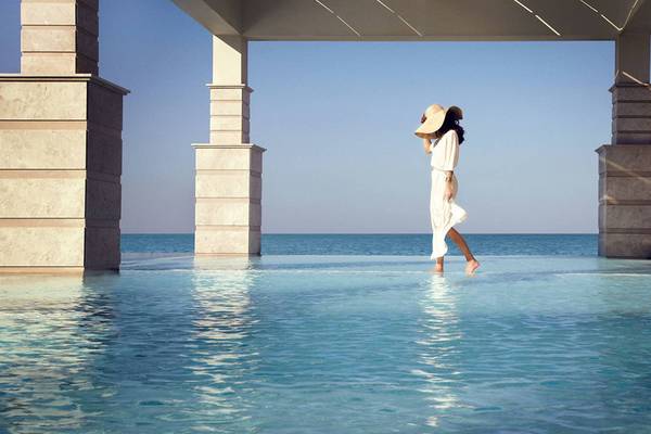 Frau im weißen Kleid und Hut geht im Pool des Jumeirah Zabeel Saray