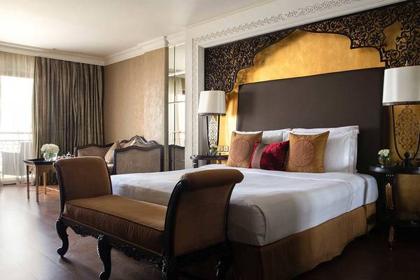 Hotelzimmer im Jumeirah Zabeel Saray mit einem großen Bett, goldenem Kopfteil und stilvollen Lampen.