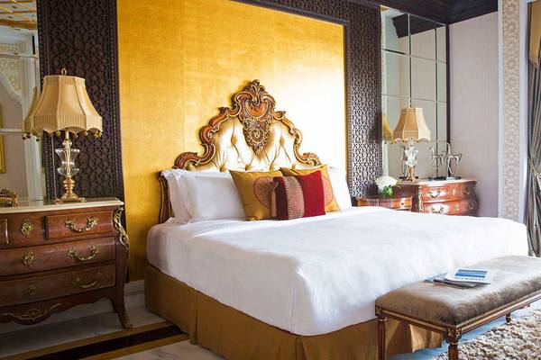 Hotelzimmer im Jumeirah Zabeel Saray mit einem großen Bett, goldenen Wänden und zwei Lampen auf Nachttischen.