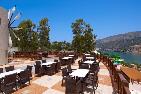 Terrasse des Fodele Beach & Water Park Holiday Resort mit Tischen und Stühlen und Blick auf Wasserrutsche und Meer