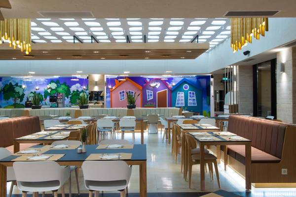 Innenansicht des Restaurants im Fodele Beach & Water Park Holiday Resort mit bunten Wandmalereien und gedeckten Tischen.