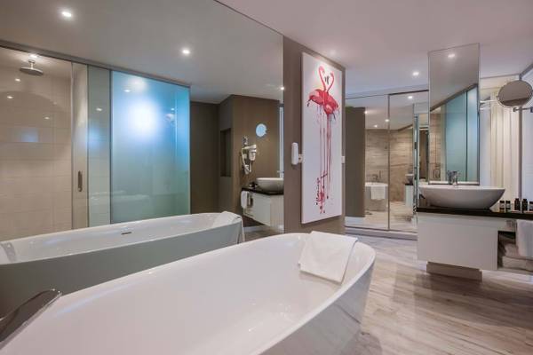 Modernes Badezimmer mit zwei Badewannen, Waschbecken, und Flamingo-Wandbild im Fodele Beach & Water Park Holiday Resort.