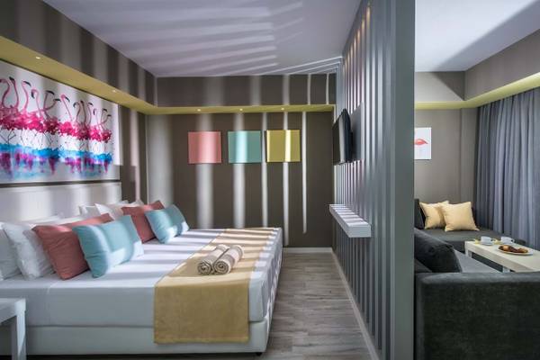 Hotelzimmer im Fodele Beach & Water Park Holiday Resort mit einem großen Bett, bunten Kissen und Kunstwerken an der Wand.