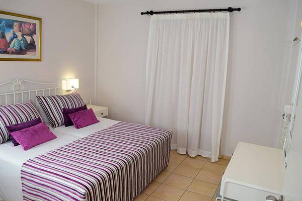 Ein modernes Schlafzimmer im Aktea Beach Village Hotel mit einem Doppelbett, farbigen Kissen und weißen Vorhängen.