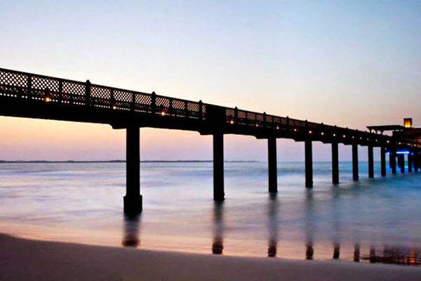 Dämmerung über der Jumeirah Dar Al Masyaf Pier mit beleuchteten Säulen im Wasser