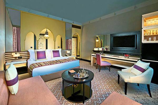Innenansicht einer Suite im Jumeirah Dar Al Masyaf Hotel mit Bett, Schreibtisch und Fernseher.