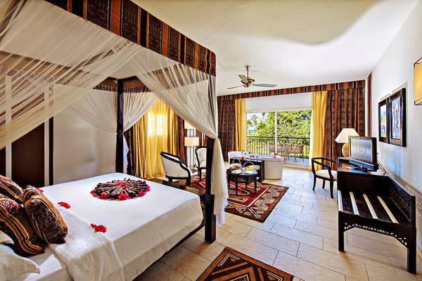 Innenansicht der Suite im Bahari Zanzibar Hotel mit Himmelbett, Balkon und Wohnzimmermöbeln.