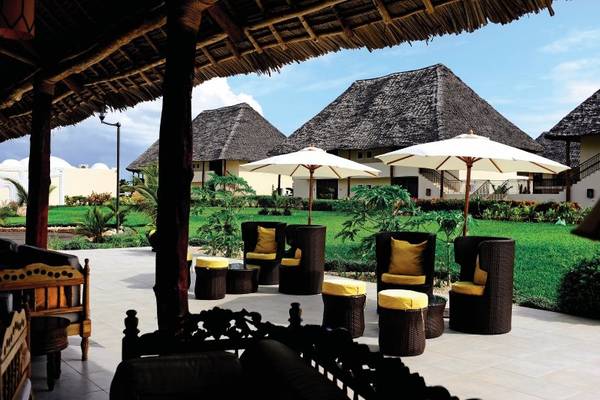 Außenbereich des Bahari Zanzibar Hotels mit Korbstühlen, Kissen und Sonnenschirmen.